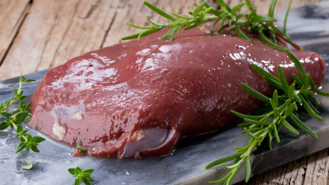 close up of a piece of beef liver on a kitchen countertop with some herbds