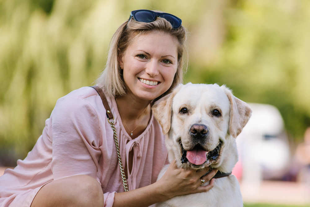 A beautiful woman is sitting near her labrador retriever on the grass in the park.